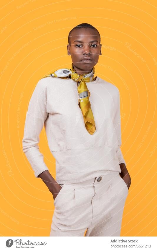 Black woman in trendy attire wearing scarf isolated on yellow background slim casual attire neck hands in pockets african american posing confident tie knot