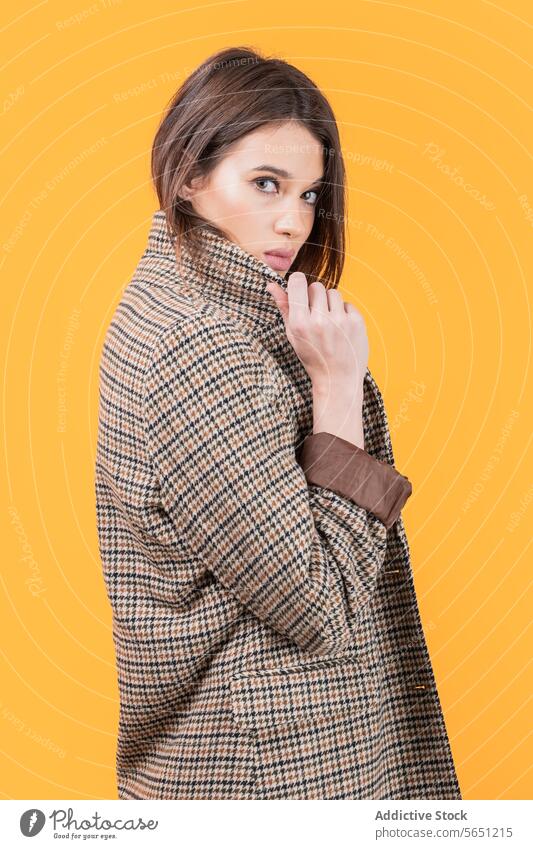 Fashionable woman in trendy coat isolated on yellow background attractive long coat checked pattern fashionable standing looking at camera confident elegance