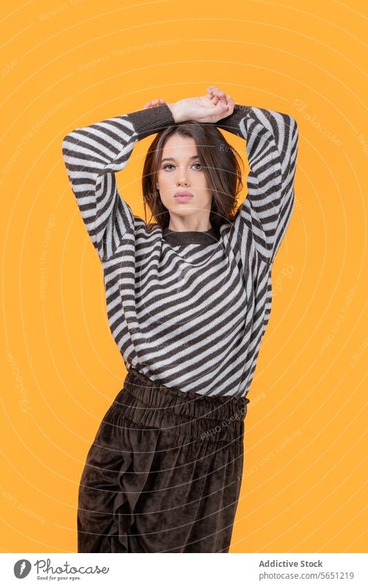 Trendy woman with hands on head isolated on yellow background trendy casual attractive looking at camera fashionable striped pattern standing confident portrait