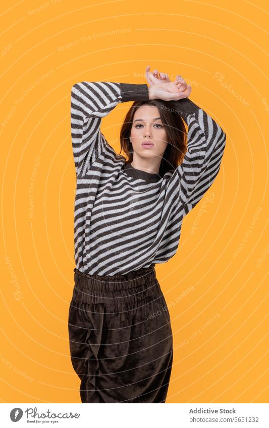 Trendy woman with hands on head isolated on yellow background trendy casual attractive looking at camera fashionable striped pattern standing confident portrait