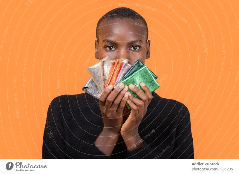 Black woman with colorful wallets isolated over orange background multicolor shiny african american holding portrait short hair money variation hand fashion