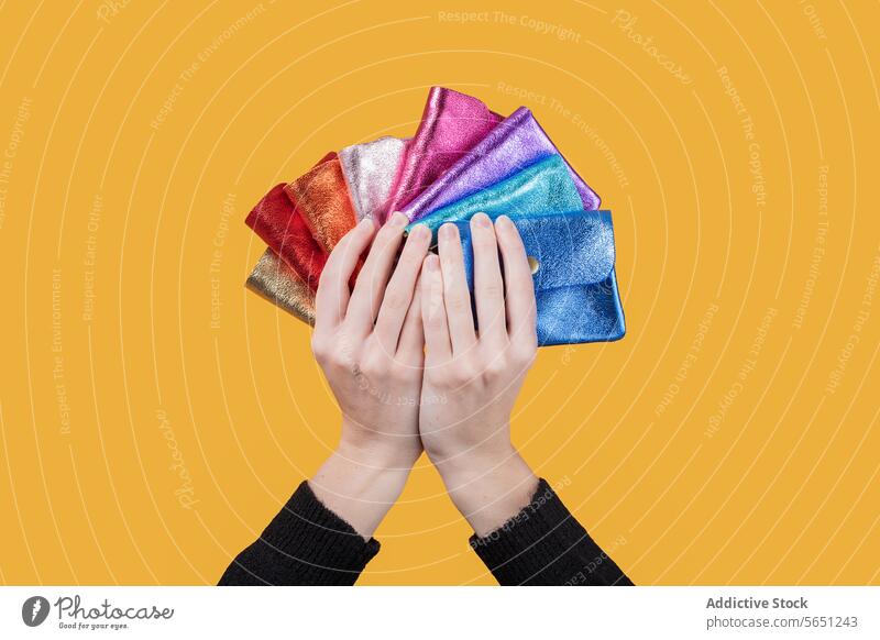 Woman holding colorful wallets against yellow background woman shiny multicolor crop hand variation isolated part of money female body part showing new finance