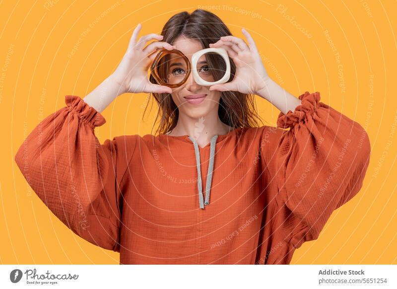 Woman making eyeglasses shape with bangles in studio woman smile casual attire looking at camera holding trendy fashionable content accessory yellow background