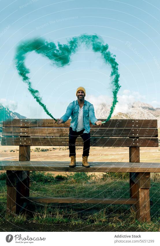 Man with heart-shaped smoke creating a whimsical scene man bench green joy happiness scenic mountains landscape nature love concept creative denim style wooden