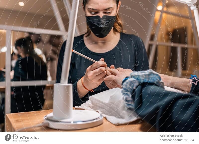 Focused young female beautician in mask doing manicures in at beauty salon women nail professional client work colleague pandemic small business process safety