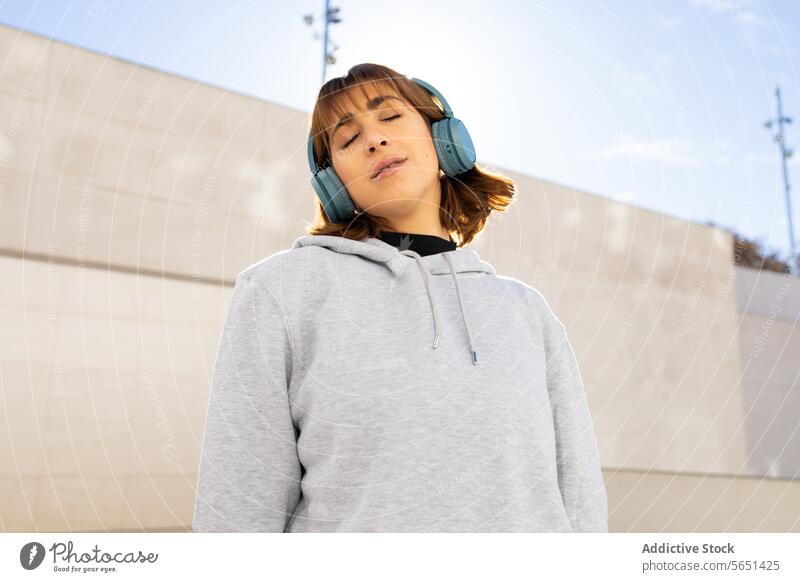 Relaxed woman enjoying music with blue headphones relaxation contentment enjoyment urban grey hoodie serene young closed eyes leisure lifestyle electronic