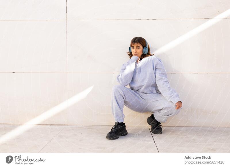 Young woman relaxing in casual attire with headphones young music tracksuit blue sneakers minimalist background sitting listening leisure comfortable fashion