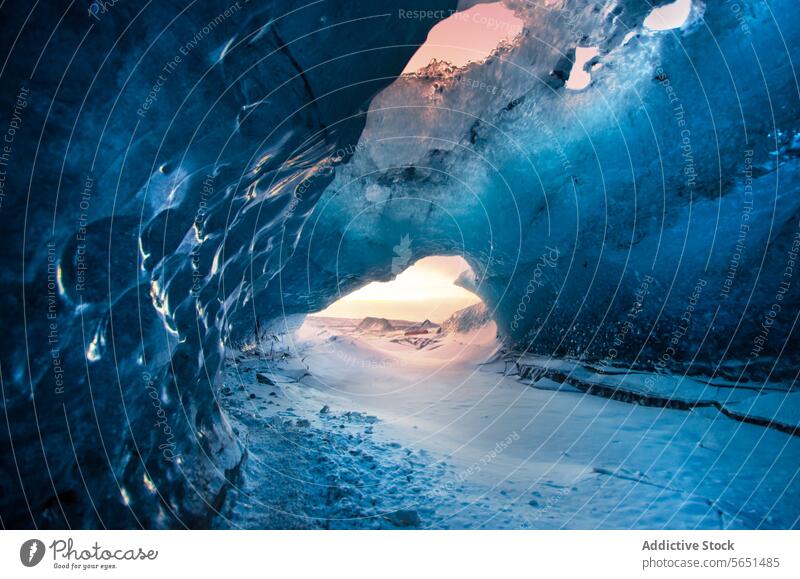 Inside view of a crystal blue ice cave in Iceland with a sunset visible through the opening. glacier interior nature arctic frozen winter icy landscape travel