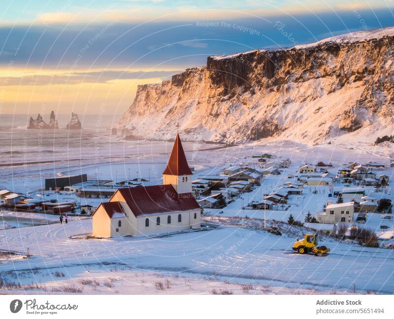 Sunset casting a warm glow over a small Icelandic village with a church nestled between snowy cliffs and the sea sunset landscape winter light architecture