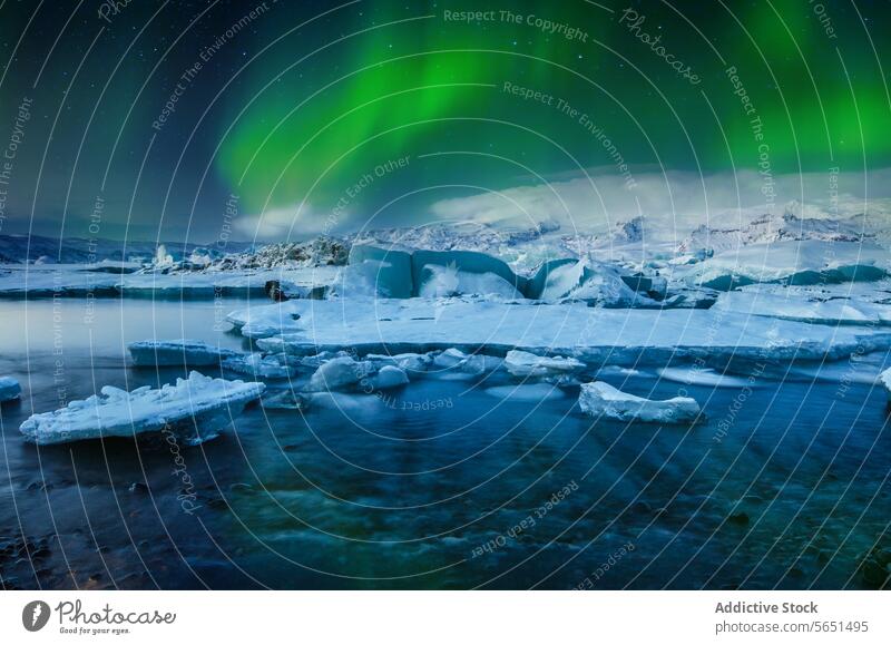 Northern lights dancing above a glacial lagoon with icebergs and snow-covered mountains in Iceland northern lights aurora night sky green natural phenomenon