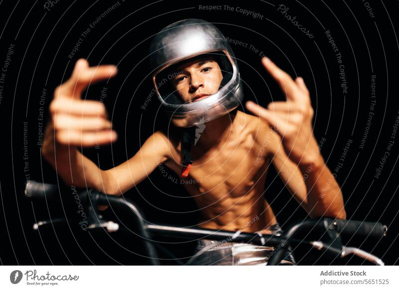 Unrecognizable young shirtless man sitting on bicycle in lights and showing devil horns gesture stuntman helmet cyclist handlebar protect rock and roll vehicle