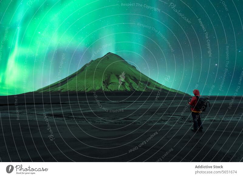 Back view of unrecognizable person standing before a volcano under the vibrant aurora borealis in Iceland northern lights observer figure silhouette night sky