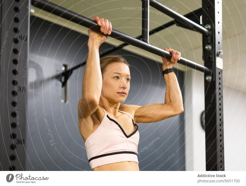 Determined woman performing pull-up exercise at gym strength endurance workout athlete fitness training health sport active determination modern indoor bar hang
