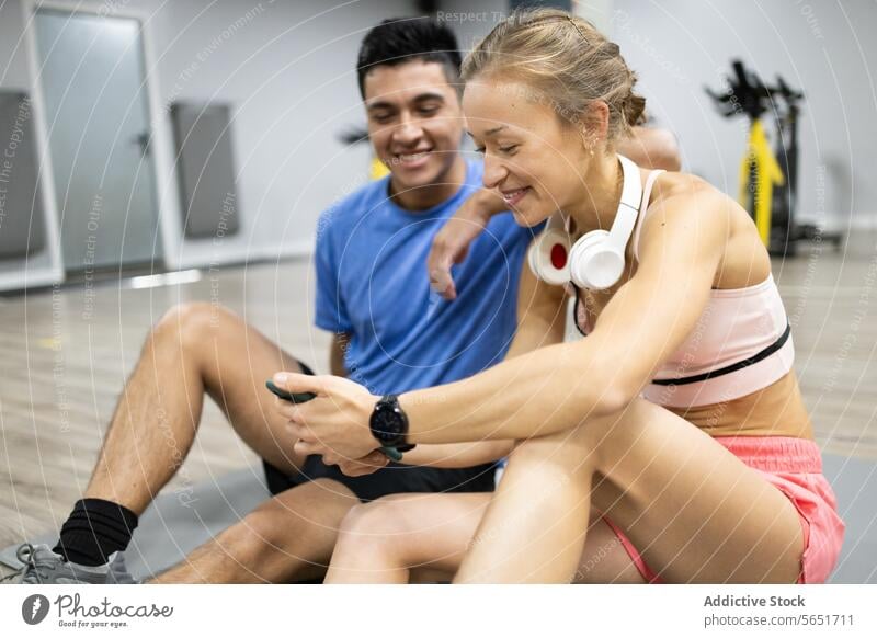 Fitness partners resting and sharing a laugh at the gym fitness workout man woman sitting floor exercise companionship active lifestyle sportswear athletic
