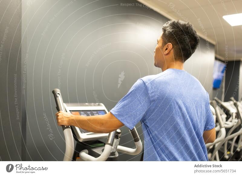 Man preparing for a workout on a treadmill in a gym man exercise fitness preparation stationary blue t-shirt side view health wellness gym equipment training