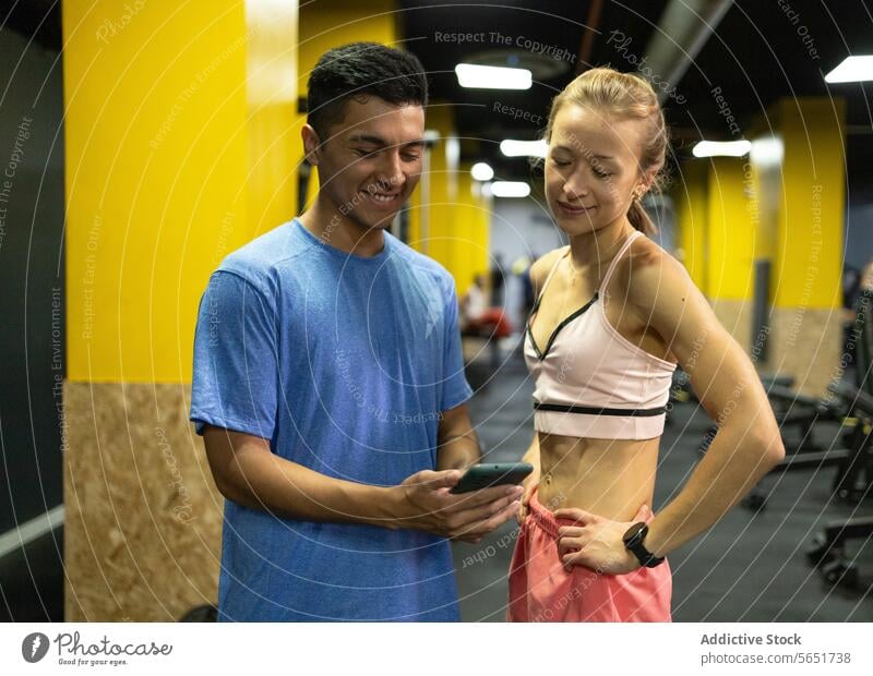 Fitness enthusiasts sharing a phone screen at the gym fitness app cheerful gym-goers man woman smartphone vibrant fitness center technology exercise workout