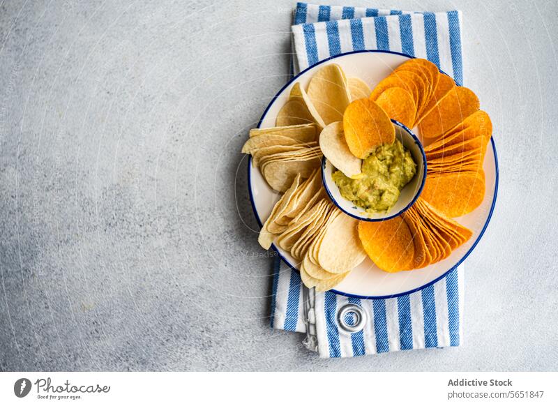 Assorted crisps with guacamole in concrete background Crisps potato paprika cheese avocado sauce snack plate bowl striped napkin appetizer gourmet dipping