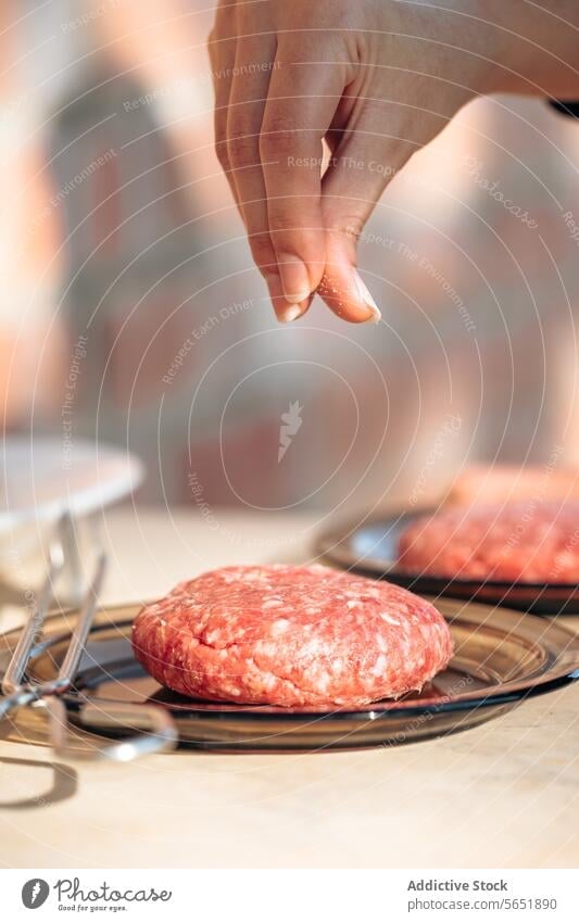 Seasoning a Patty for Grilled Burgers hand seasoning salt sprinkling burger patty raw prepping grilling close-up meat cooking preparation beef kitchen food