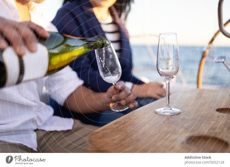 Crop couple pouring champagne into wineglasses on yacht alcohol sailboat date sea romantic love relationship table drink beverage celebrate bottle restaurant