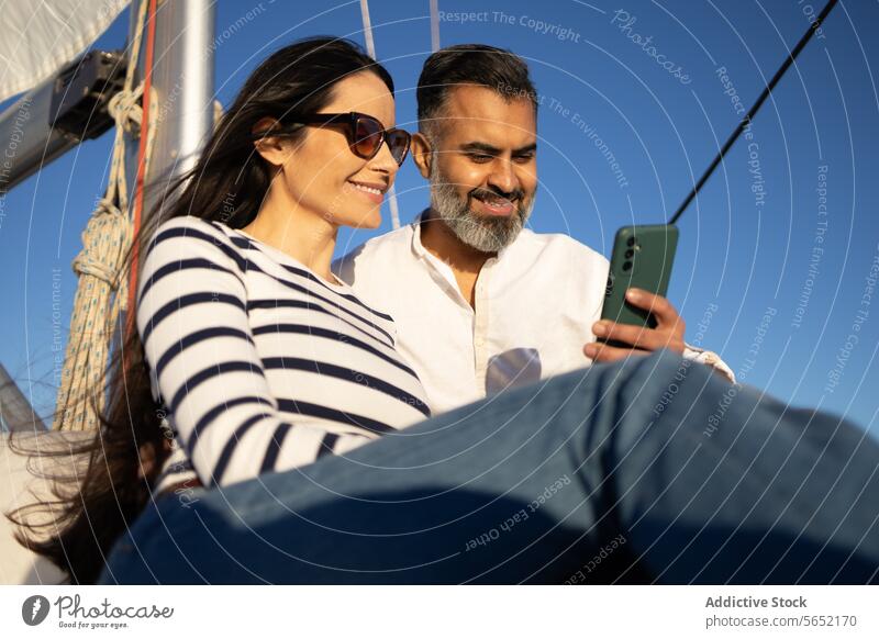Smiling couple browsing smartphone while sitting on yacht using smile surfing mobile device vacation happy travel cellphone enjoy internet romantic pleasure