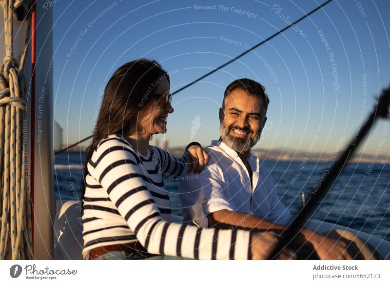Smiling couple sitting on yacht smile pleasure enjoy relax sea happy trip romantic peaceful lifestyle casual adventure paradise embrace hug sailboat tourism