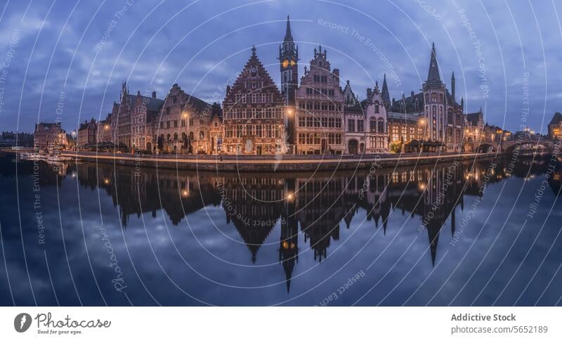 The historic buildings of Ghent are mirrored in the calm waters during twilight, showcasing the city's medieval charm reflection Belgium cityscape