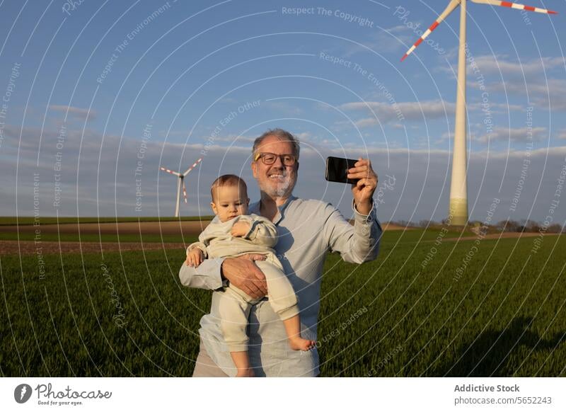 Happy grandfather taking selfie with grandson on wind farm Grandfather Grandson Smartphone Windmill Smile Selfie Nature Cute Together Love Futuristic Renewable