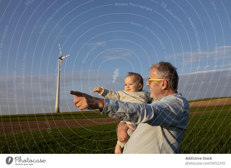 Happy grandfather showing something to cute baby boy on wind farm Grandfather Grandson Windmill Pointing Finger Showing Nature Smile Cute Together Love