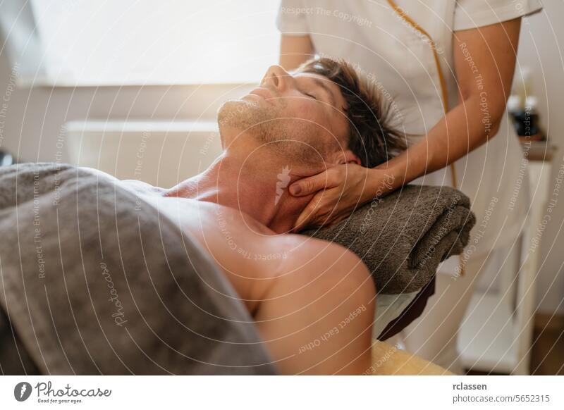 Therapist giving a neck massage to a male client in a bright spa room physiotherapist hotel massage oils asian relaxation therapist's hands wellness
