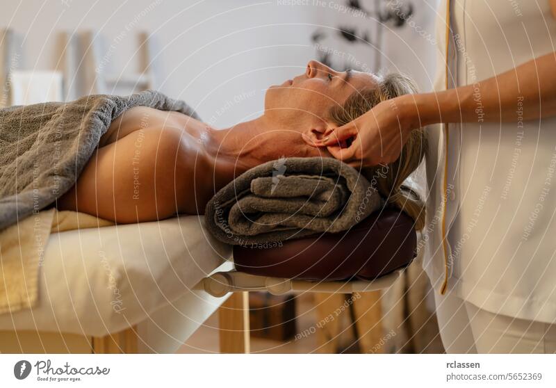 Side view of a massage therapist doing an ear massage for a relaxed female client hotel asian beauty salon head woman relaxation therapist's hands
