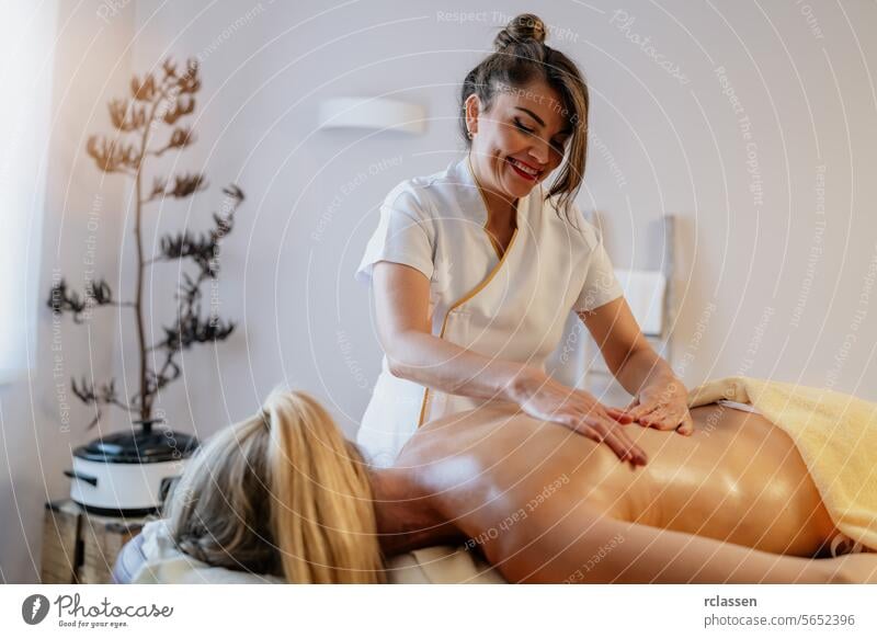 Smiling asian massage therapist giving a back massage to a relaxed client in a spa hotel resort massage oils physiotherapist beauty salon relaxation wellness