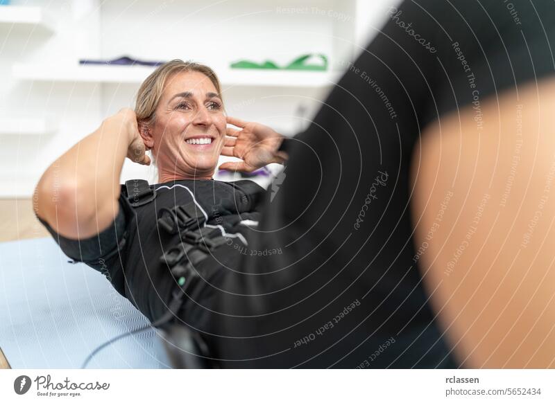 Woman smiling while doing sit-ups in an EMS training suit at a gym neuromuscular ems training suit woman fitness exercise personal training trainer celebrating