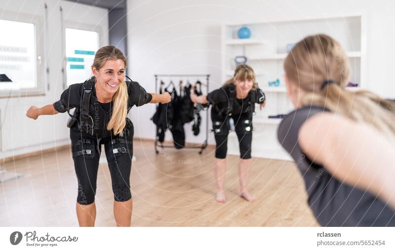 Two women in EMS training suits doing balance exercises front of a trainer in a gym electro stimulation neuromuscular electrical endurance body sculpting