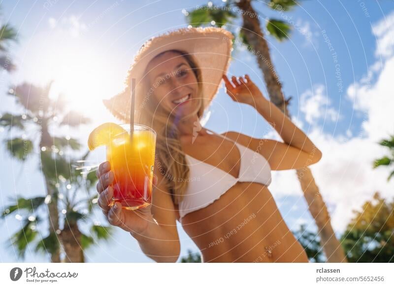 Smiling woman in white bikini and straw hat holding a tropical cocktail, palm trees, sunny sky at caribbean island party smiling woman vacation leisure summer