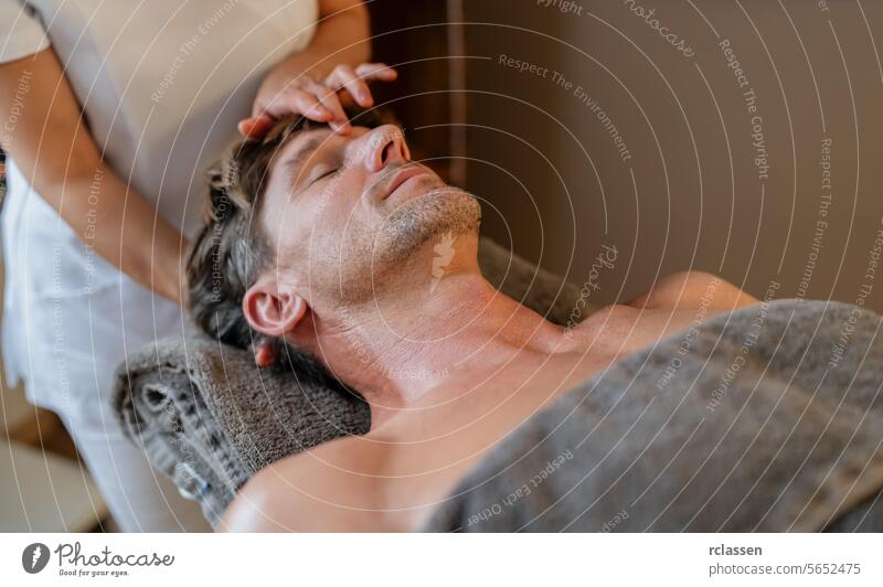 Man relaxing during a head massage in a spa with therapist's hands on forehead male patient wellness stress relief body care tension relief healing touch