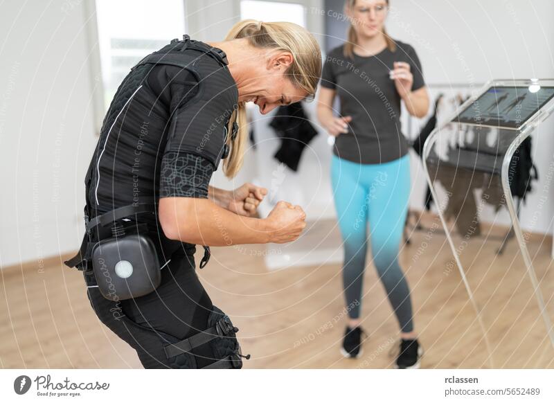 Woman in EMS suit performing exercises with trainer guidance in a gym electro stimulation neuromuscular electrical ems suit woman exercising
