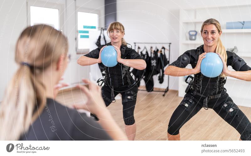 Women exercising with blue gym balls in front of a trainer in a training session and wearing EMS training suits at a EMS-Studio. black suit black suits