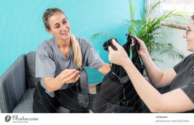 Trainer holding an EMS training vest while talking to a client in a EMS - Studio ems training vest woman trainer consultation room conversation armchairs indoor