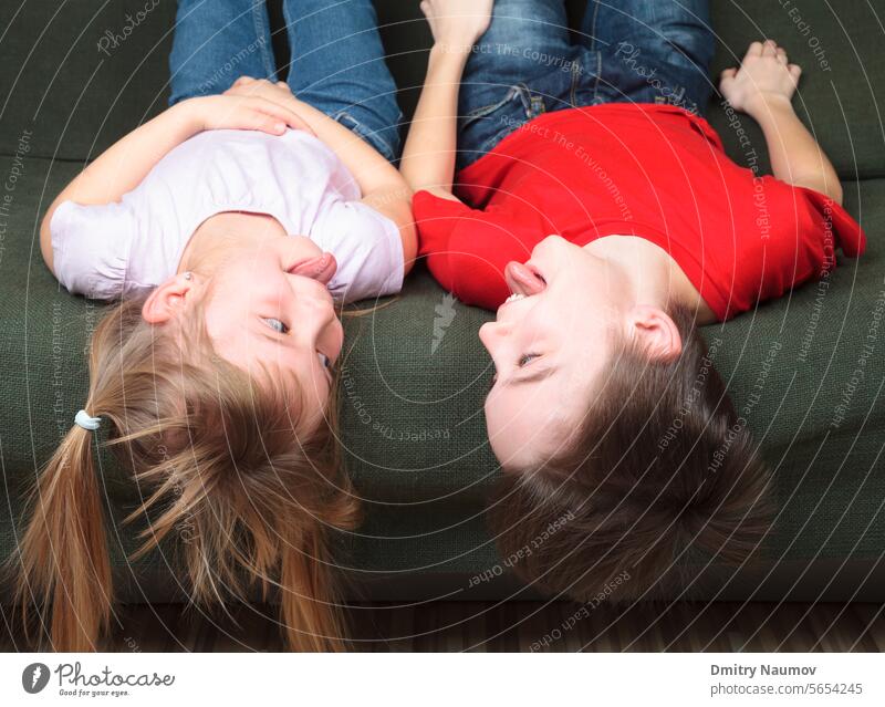 Brother and sister  wearing casual clothes laying on a green sofa at home stick out tongues teasing each other Half-sibling arguing bad behavior boy brother