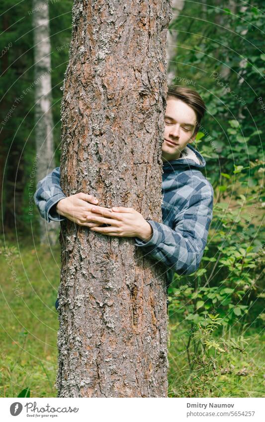 Teen boy hugs pine tree in a forest activist candid care concept connect conservation ecology embrace environment environmentalist eyes closed forestation hands