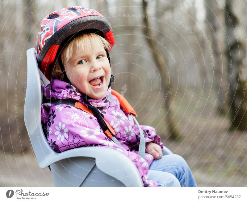 Happy little girl wearing helmet sitting in bycicle child seat 2 years autumn baby bicycle bike biker biking caucasian chair cheerful childhood cute cycling