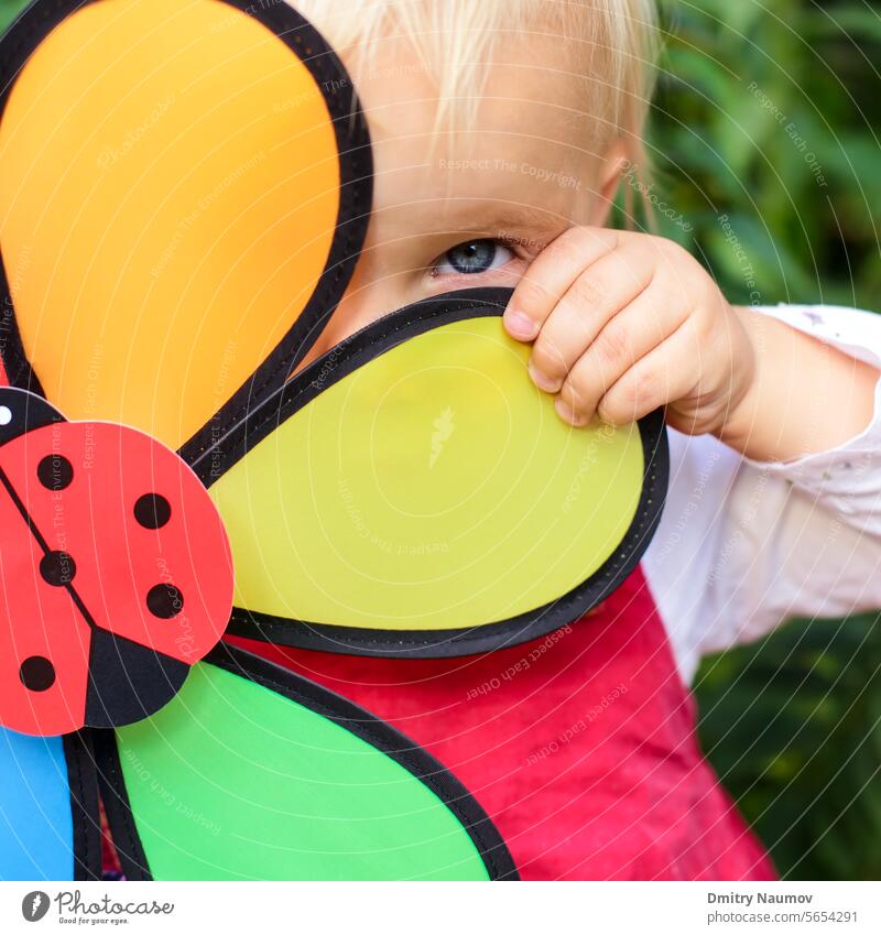 Portrait of cute little girl hiding behind flower toy outdoors 2 years attractive beautiful blonde caucasian child childhood face fun game green hair happy