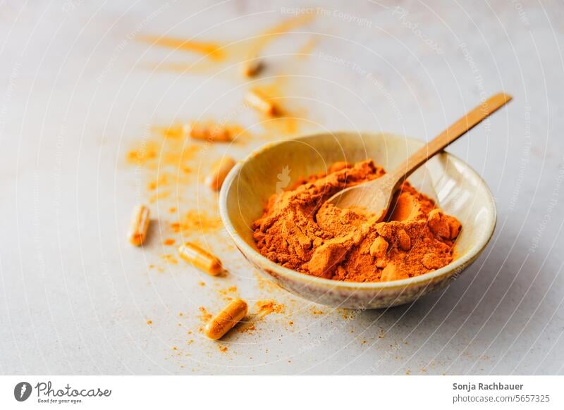 Turmeric powder in a bowl with a wooden spoon and capsules on a gray table. turmeric Powder Close-up Spoon Food seasoning Healthy Aromatic medicine