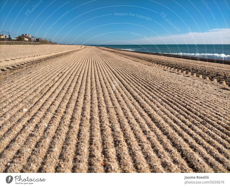 Vilassar de Mar beach, Barcelona. With many long straight lines that disappear into the horizon (the lines are the marks of the tractor that cleans the sand) on the right hand side the Mediterranean Sea, day with blue sky, first thing in the morning.