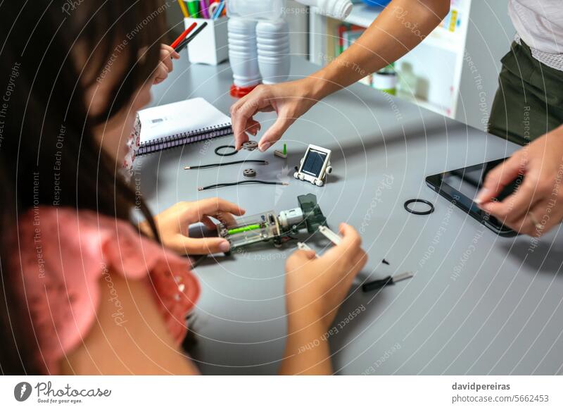 Female teacher helping girl students to assemble pieces of machine in a robotics class unrecognizable female explaining child electronic electrical connect