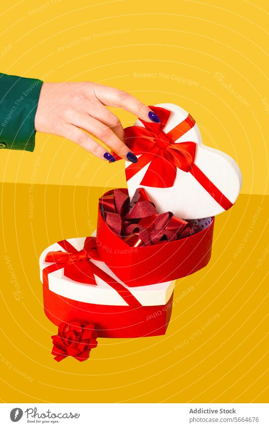 Anonymous hand opening a heart-shaped gift box with red ribbons on a yellow background Hand present valentine love celebration festive decoration elegant