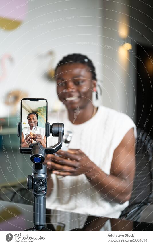 Cheerful black man records a skincare tutorial using a smartphone and gimbal with a modern interior background recording cheerful vlog broadcasting video happy