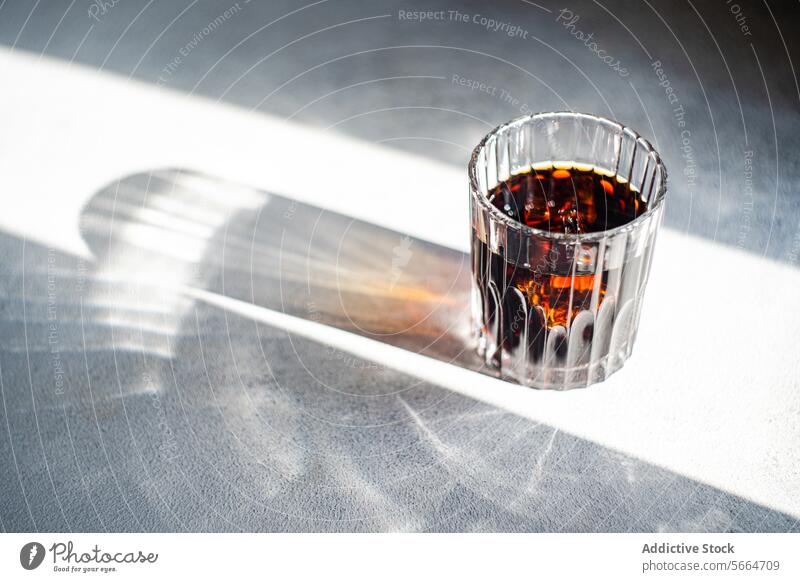 Top view of sunlight filtering through a faceted glass of cherry liqueur casting a sharp shadow on a grey surface alcohol drink beverage bright reflection red