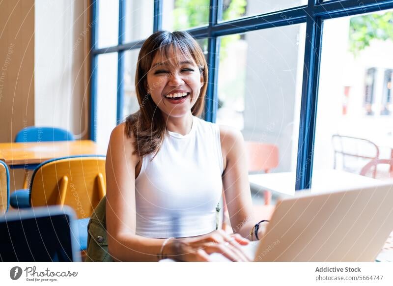 Cheerful Asian woman enjoying a remote work session in a cafe, with a bright window backdrop in Chiang Mai, Thailand cheerful happy technology business smile