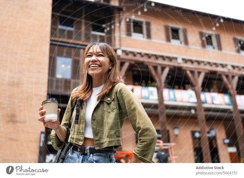 Cheerful Asian woman with a backpack and coffee cup, walking outdoors, showcasing the flexible life of remote working in Chiang Mai, Thailand joyful cheerful